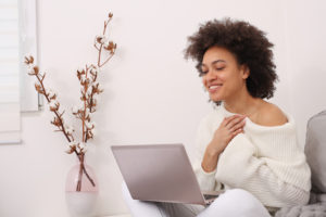 A woman smiles while using a laptop. This relates to actions that would be taken when looking for a therapist in San Diego, CA. Our therapists offer effective therapy in San Diego, CA for women, teens, and children.