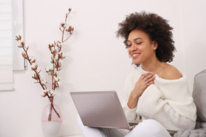 A woman smiles while using her laptop. She is happy that she started online therapy in San Diego, CA with Headway Therapy.