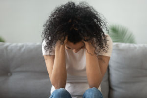 A woman sits with her head down. This is similar to topics discussed in therapy for women in San Diego, CA. Headway also provides postpartum therapy in San Diego, CA and online therapy for women in California.