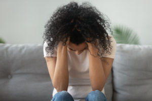 A woman sits with her head down. This is similar to topics discussed in therapy for women in San Diego, CA. Headway also provides postpartum therapy in San Diego, CA and online therapy for women in California.