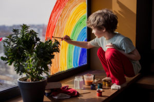 A child paints a rainbow on a window. They are feeling happy since starting child therapy in San Diego, CA. 